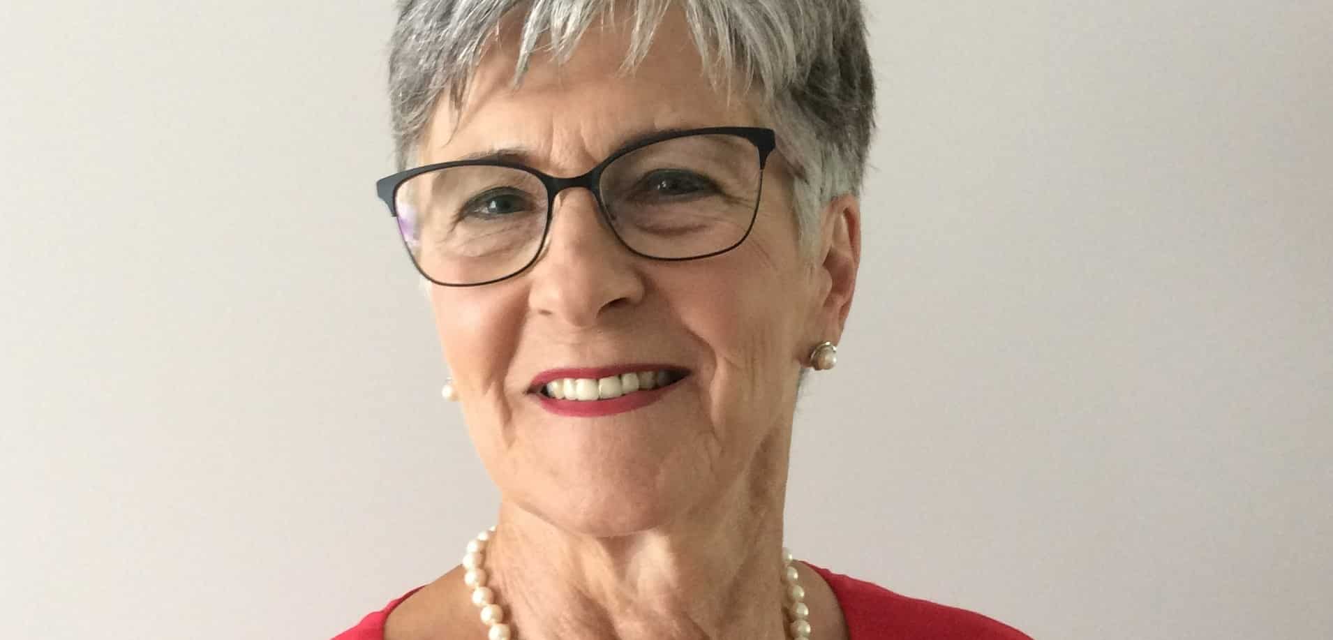 Woman wearing red shirt and pearls.