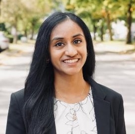 Person in blazer outdoors, smiling.