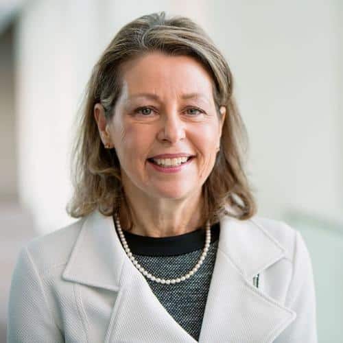 Woman in light coat with pearls.
